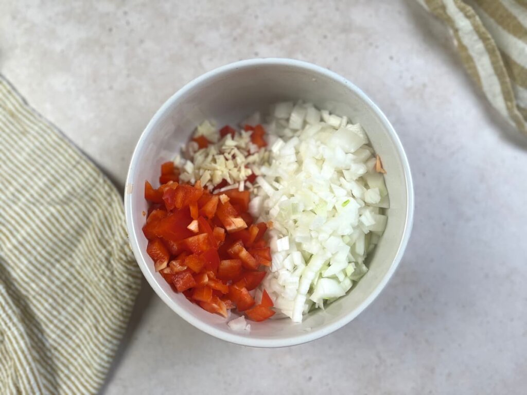 Receta arroz con setas paso 1 corta la cebolleta, el pimiento rojo y los dientes de ajo. Después, trocea las setas y el jamón