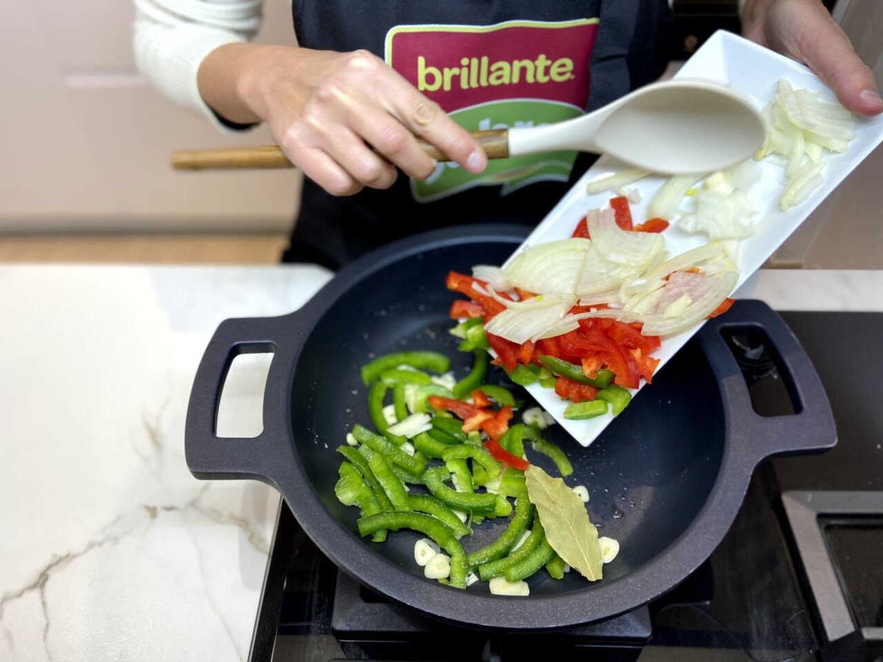 añadiendo la cebolla, el pimiento verde y el pimiento rojo a la sartén