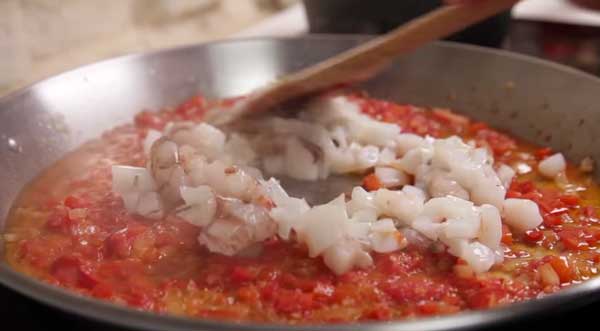 Paella en el fuego con aceite, el ajo y la cebolla, pimiento rojo y sepia