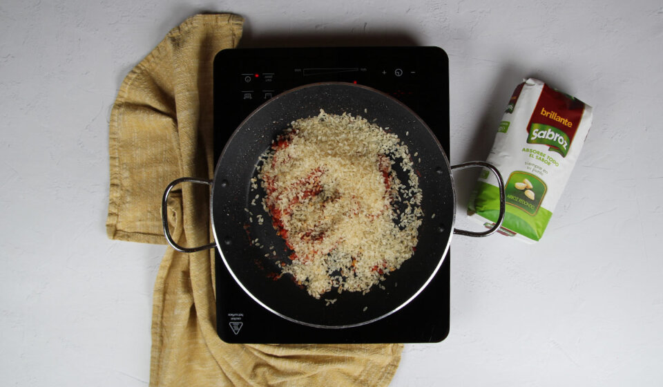 Añadir arroz a paella de secreto y alcachofas